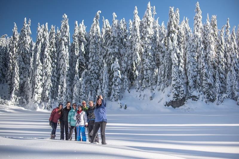 Group of people taking a selfie in a field of snow with snowy trees behind them