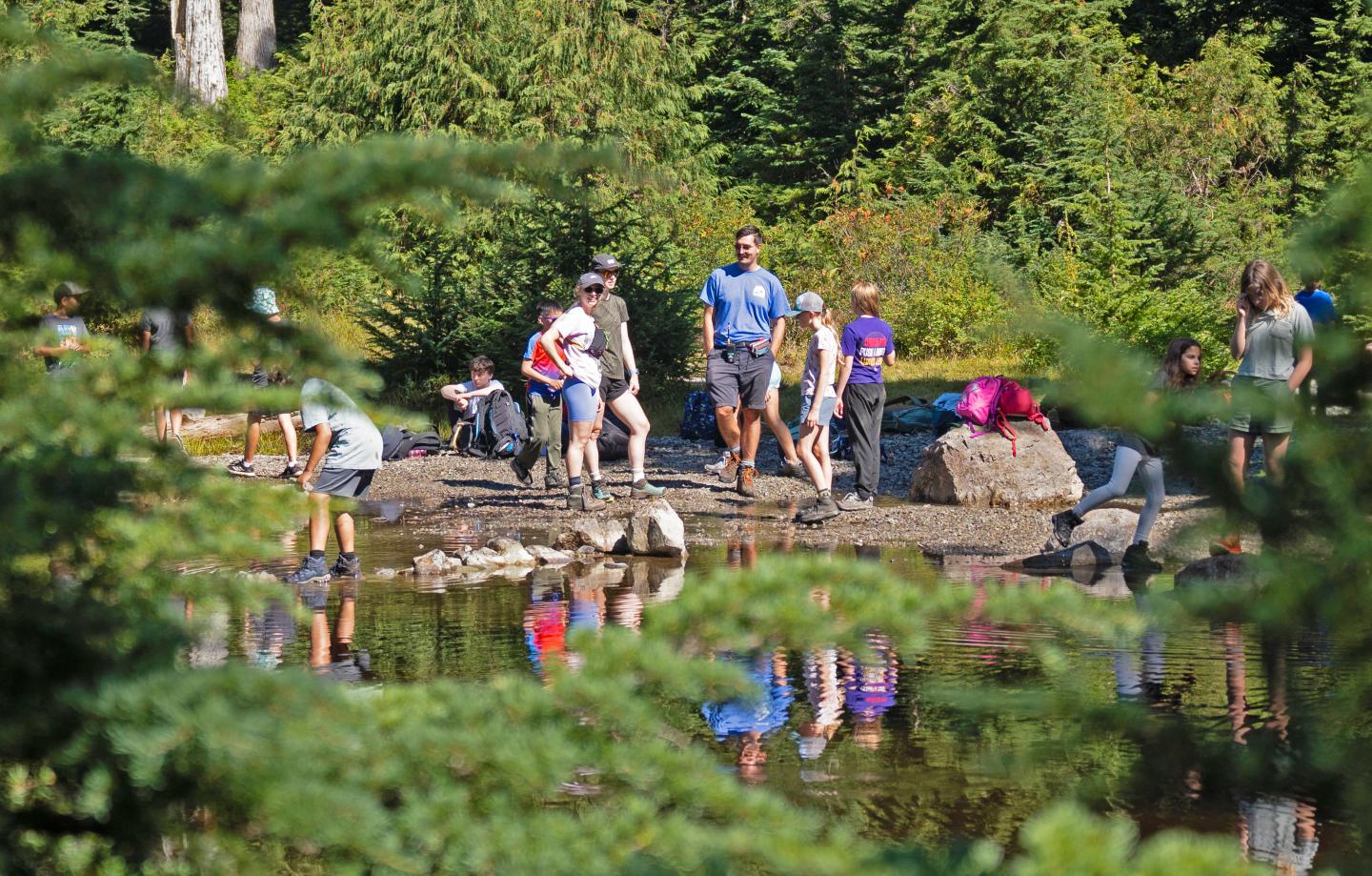 Group of people exploring a forested lakeside, with reflections in the water.