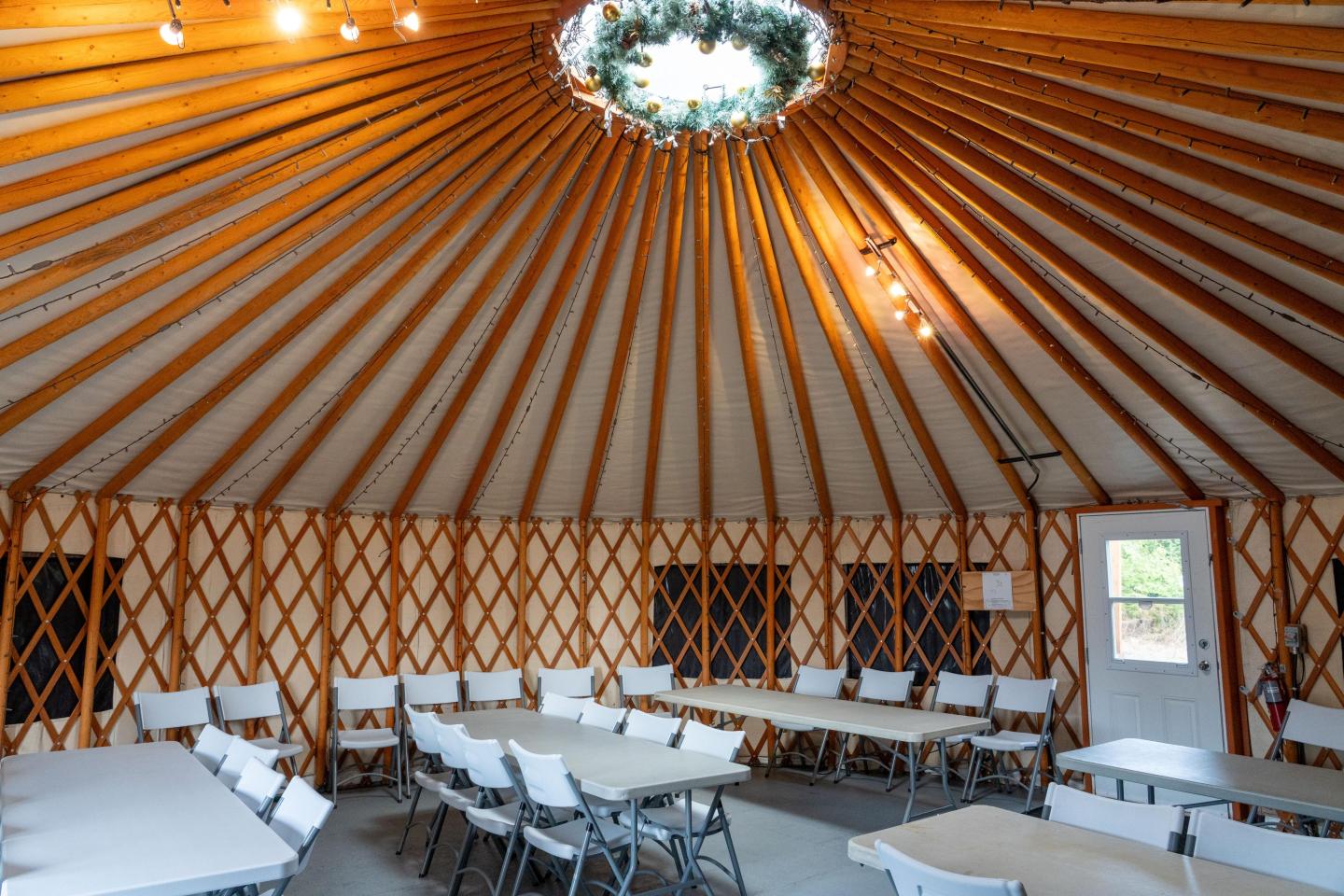 Round yurt interior, tables and chairs, warm lighting, wood lattice walls.
