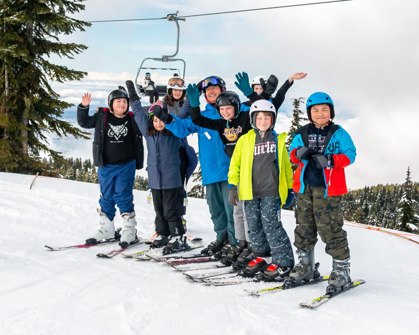Kids in ski gear posing happily on a snowy slope with trees and a ski lift in the background.
