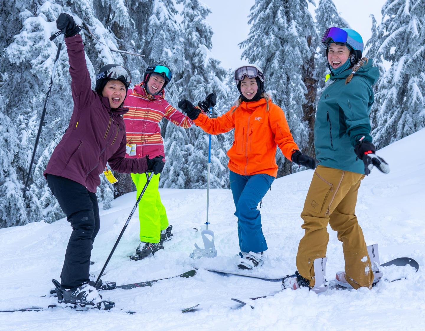 Four skiers in colorful gear cheering on a snowy mountain slope.