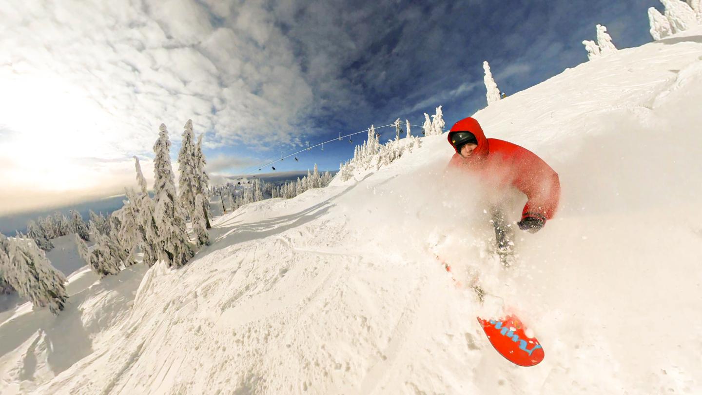 Snowboarder in red gear carving down a snowy slope under a cloudy sky.