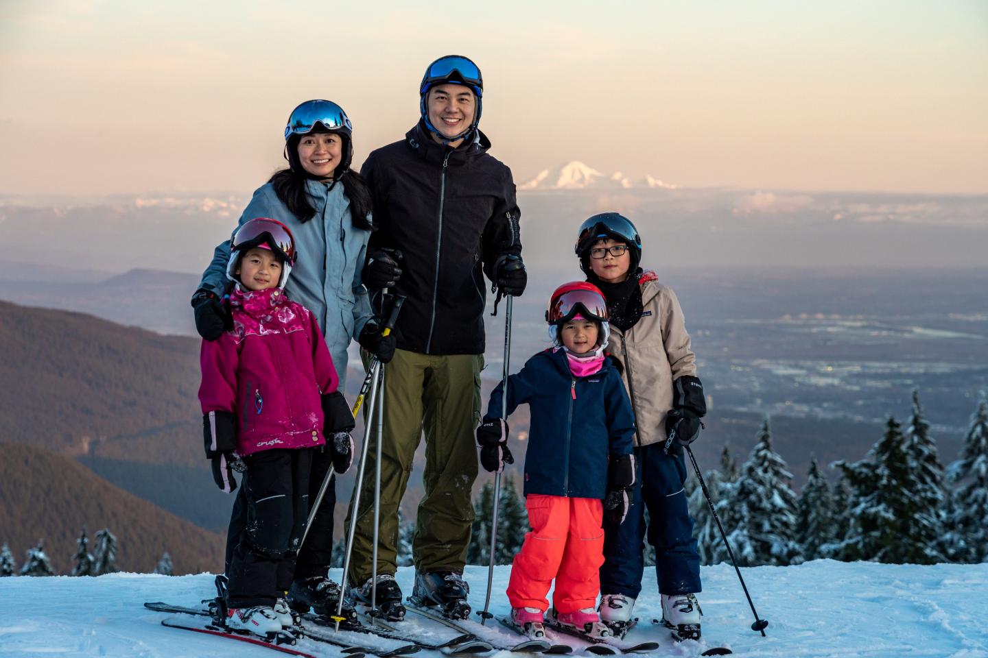 Family skiing on snowy mountain at sunset.