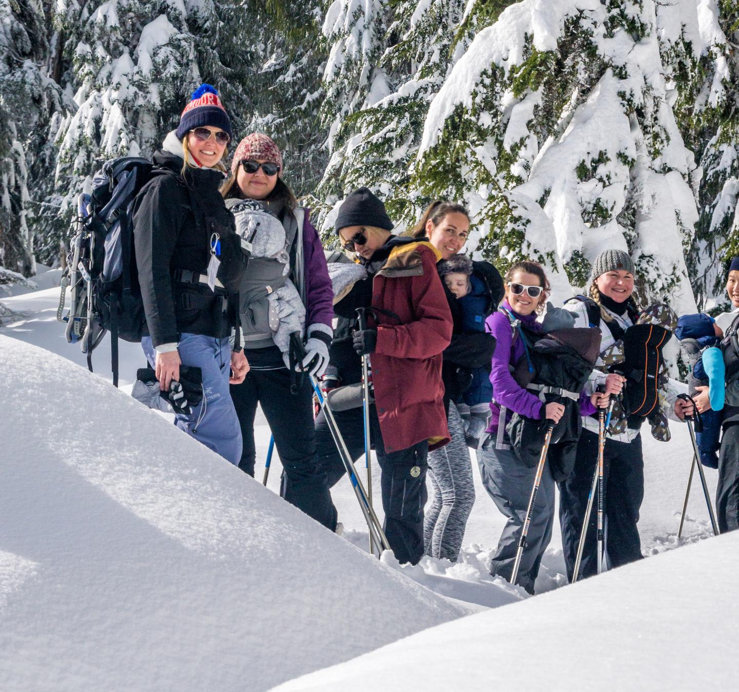 Group hiking in snowy forest with winter gear and ski poles.