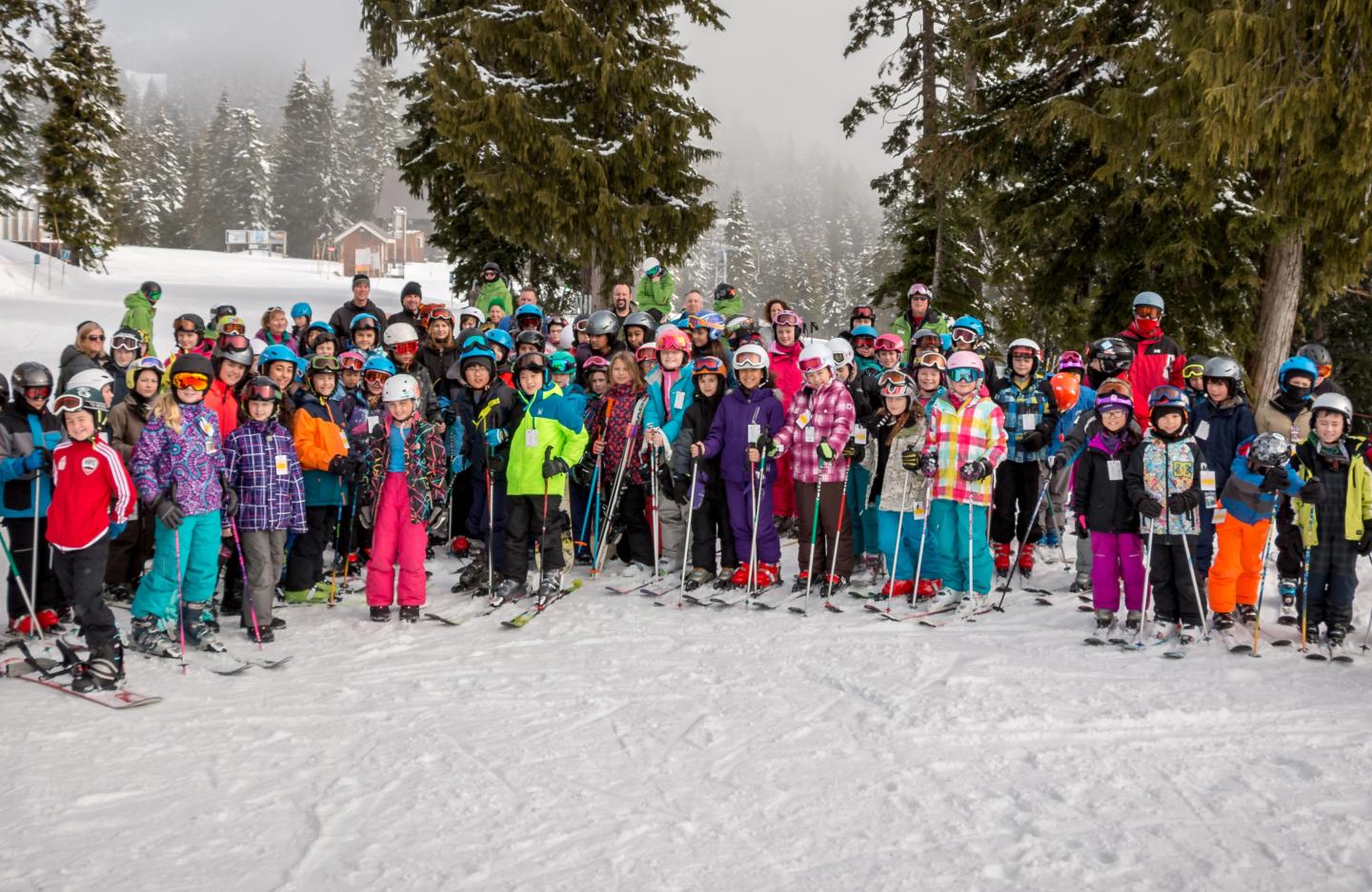 Ski group posing on snowy slope with colorful outfits, surrounded by trees.