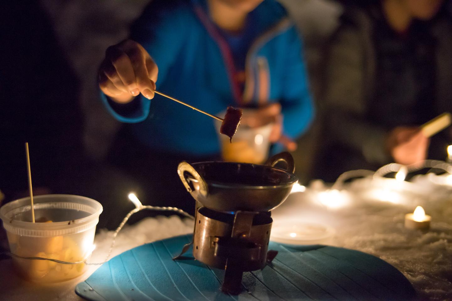 Fondue pot with skewered food, surrounded by warm lights.