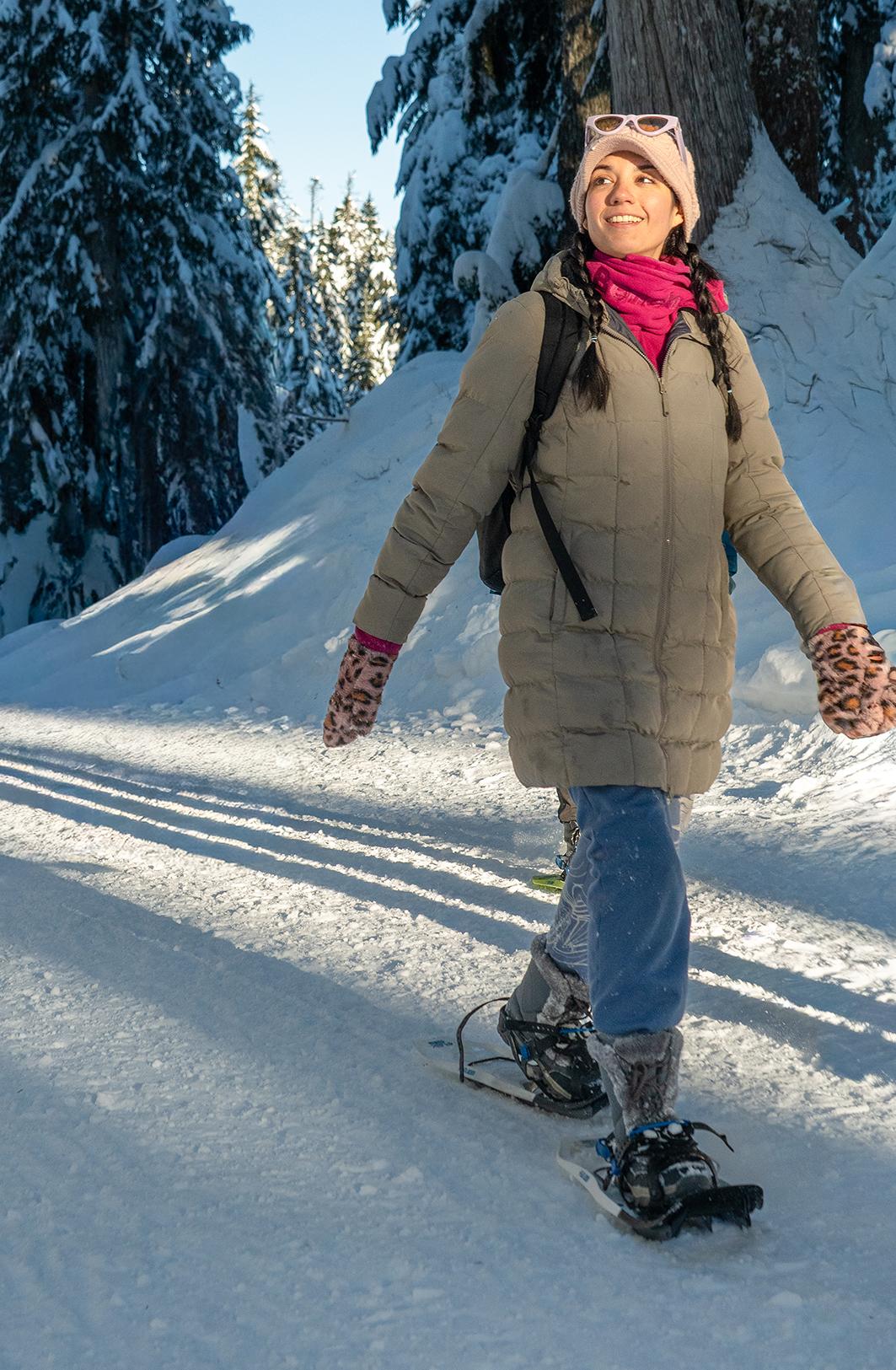 Woman snowshoeing on a sunny, snowy trail in a forest.