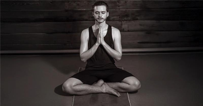 Man meditating sitting cross-legged on a yoga mat, hands in prayer position.